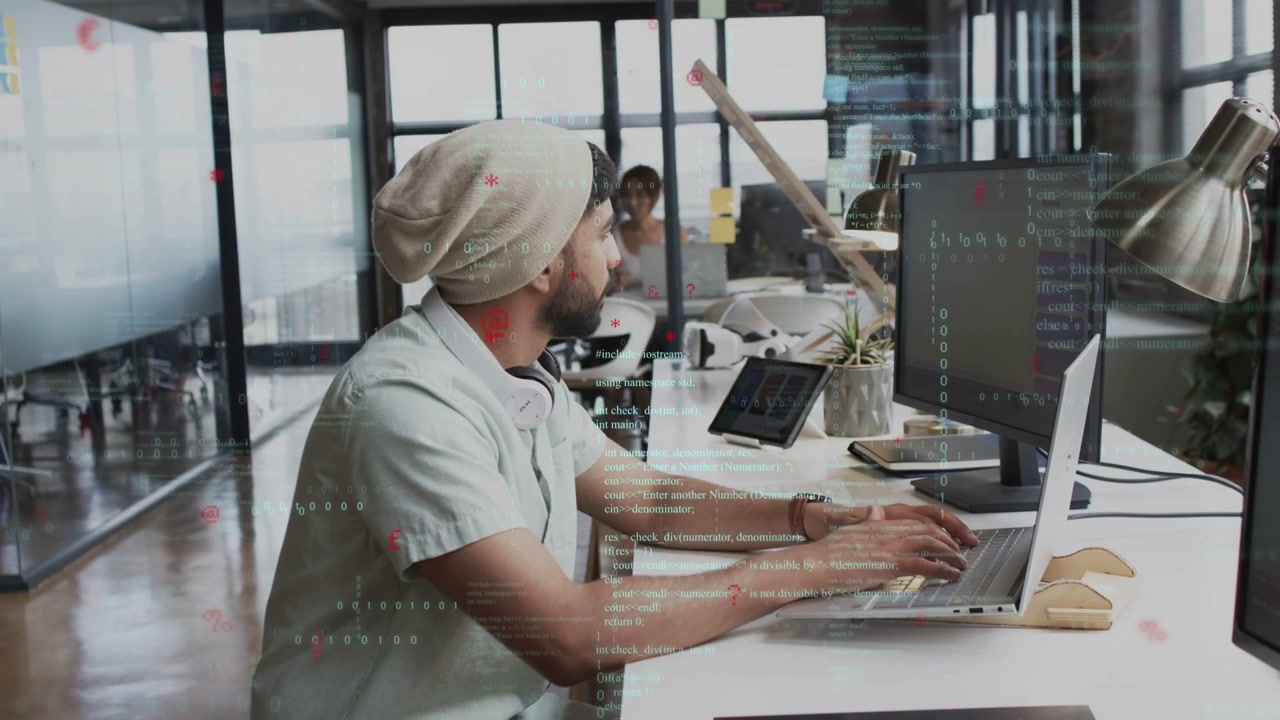 Developer typing at bench with laptop, glancing as coworker appearing, code overlay marking edits