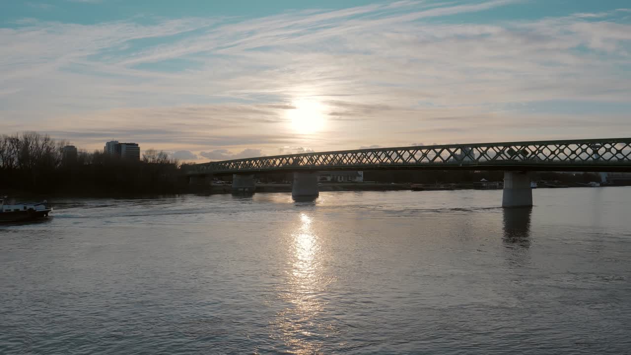 그 위를 가로지르는 다리가 있는 넓은 강의 전망과 작은 화물선이 해질녘에 지나간다