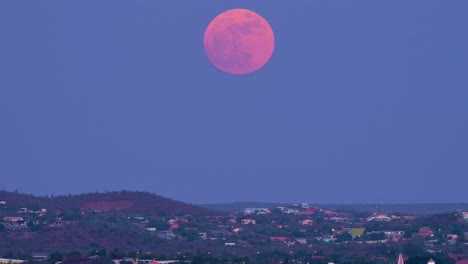 pan up across homes on hillside of willemstad curacao near janwe church to supermoon, pink and red