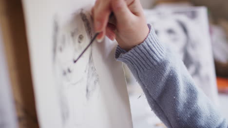 close up of artist sitting at easel drawing and picture of dog using charcoal copied from photograph