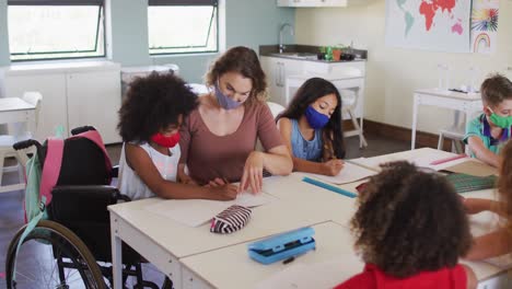 maestra que usa una máscara para la cara enseñando a una niña discapacitada en la clase