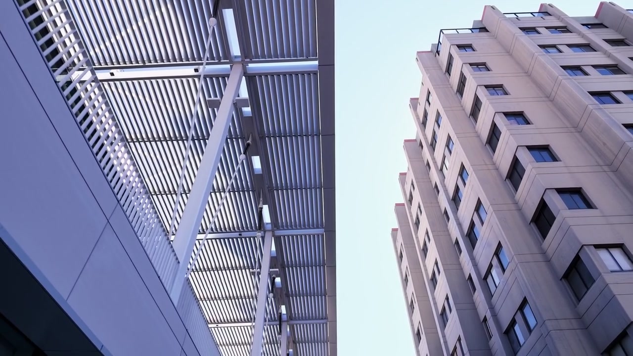 Vista pedonale dal basso che rivela la moderna architettura universitaria nel campus dell'UC Berkeley in California, mostrando facciate di edifici geometriche e un grattacielo in cemento contro un cielo sereno.