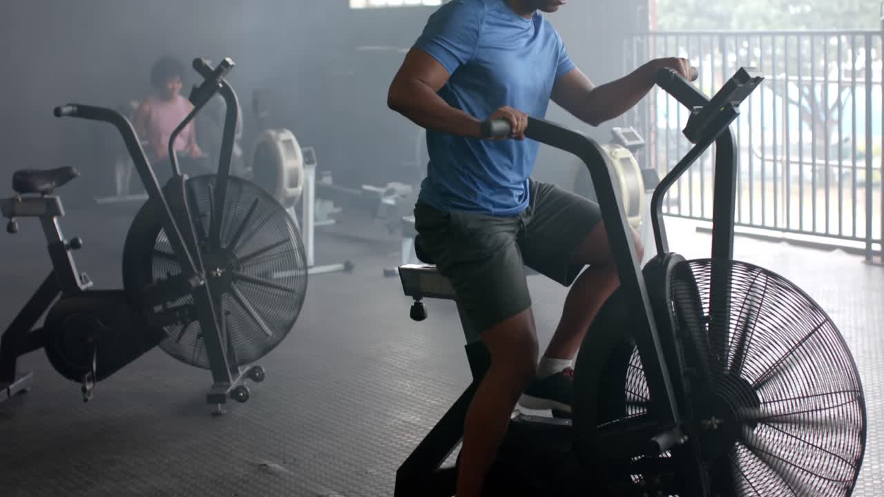hombre biracial enfocado entrenando en bicicleta elíptica en el gimnasio, cámara lenta
