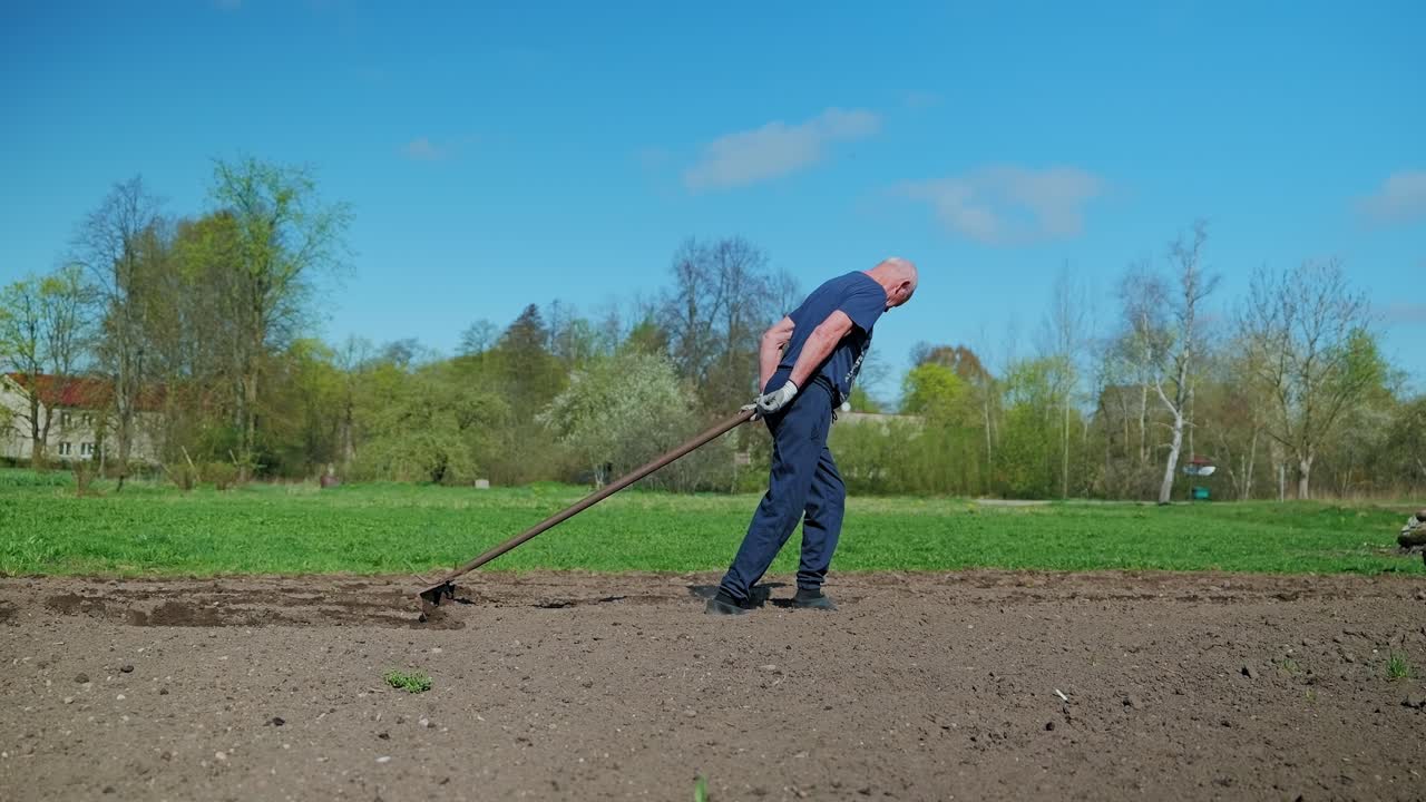 Side view slow motion shows man pulling four furrows using manual farming tool