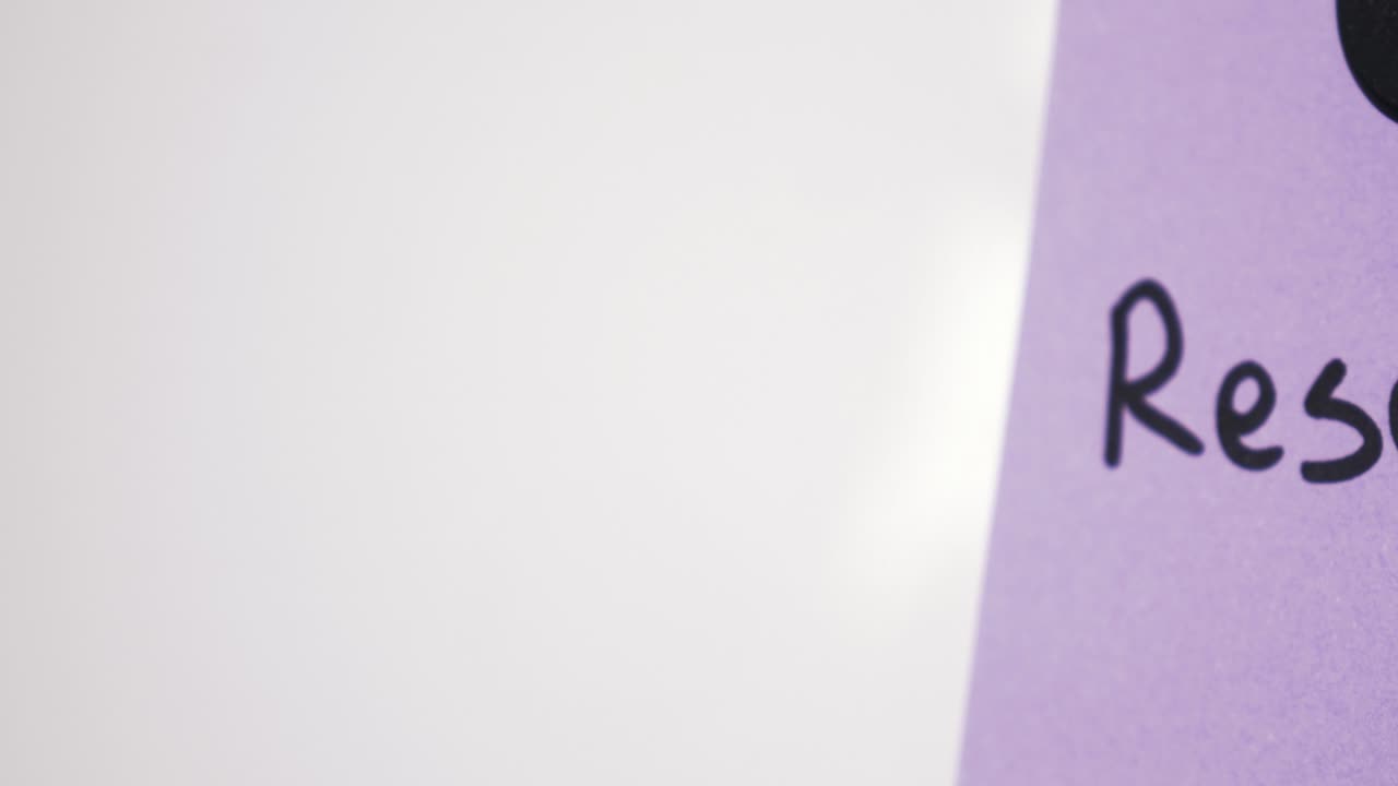 Pan reveal of Research text on purple note held by magnet on whiteboard with selective focus