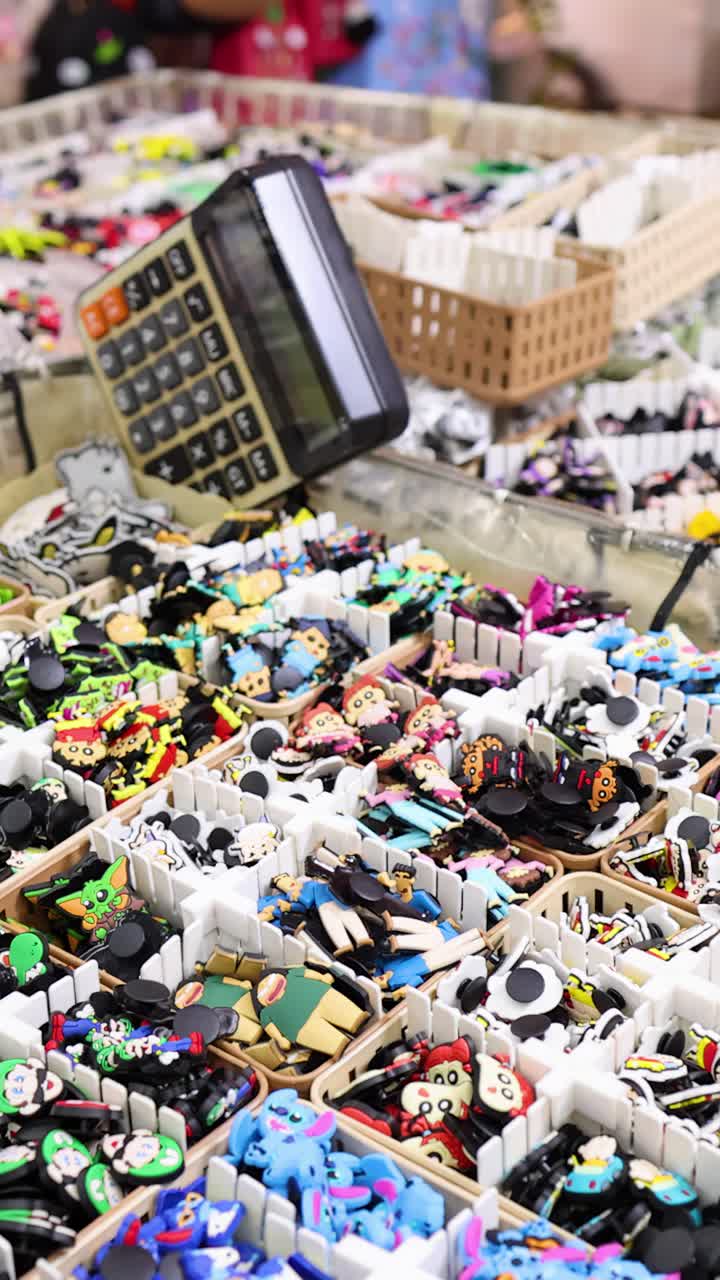 Close-up panning shot of assorted novelty trinkets and accessories at a vibrant night market stall