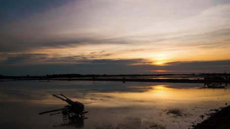 Sunset-on-reflective-water-logged-Asian-rice-paddy,-being-prepared-with-tractor-plough-in-foreground,-silhouetted-workers-in-background