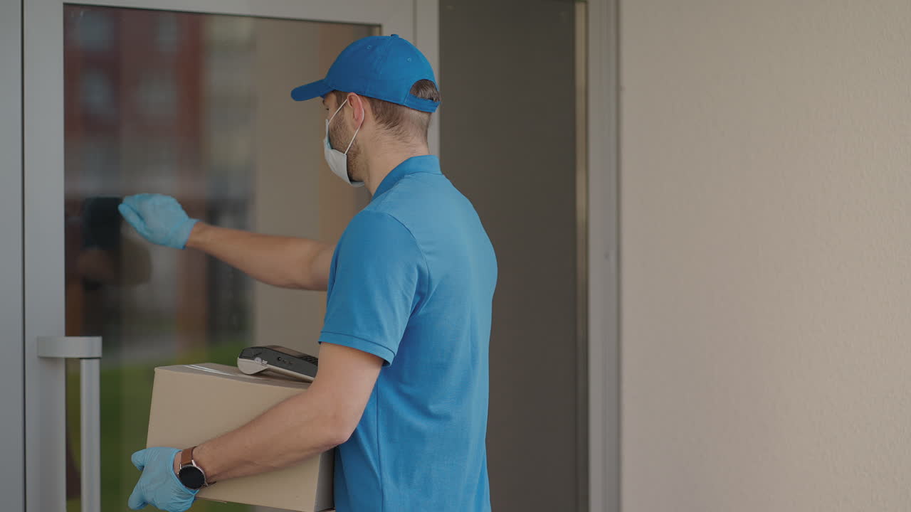 A delivery man wearing a protective mask and gloves passes the parcel to the customer and receives a contactless payment via NFC