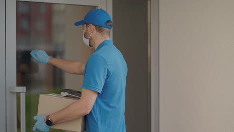 a delivery man wearing a protective mask and gloves passes the parcel to the customer and receives a contactless payment via nfc