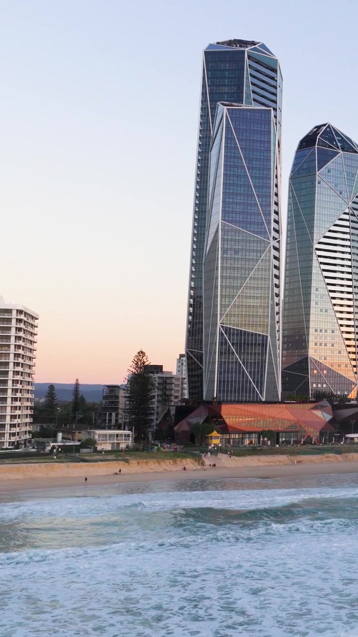 Aerial view of Gold Coast's skyline with modern skyscrapers and ocean waves at sunset, showcasing serene coastal beauty