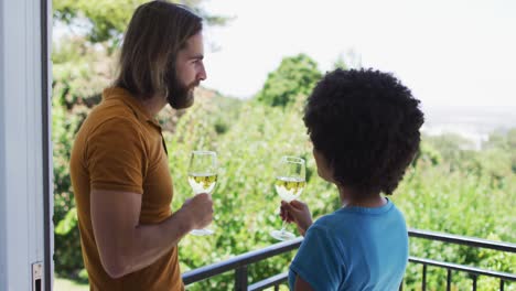 pareja de raza mixta bebiendo vino juntos mientras están de pie en el balcón en casa