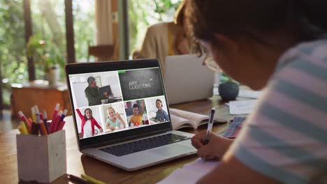 Schoolgirl-using-laptop-for-online-lesson-at-home,-with-diverse-teacher-and-class-on-screen