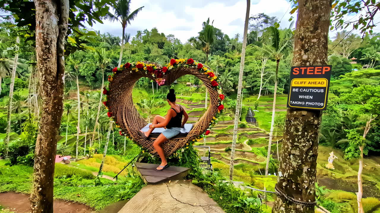 profile view of a woman sitting inside heart shaped sitting area with a view of dense, green foliage and greenery n Tegallalang rice terrace in Bali, Indonesia