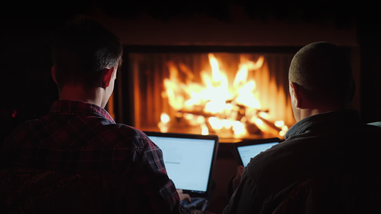 벽난로 옆의 겨울 저녁 - 남자들은 노트북과 태블릿을 사용한다