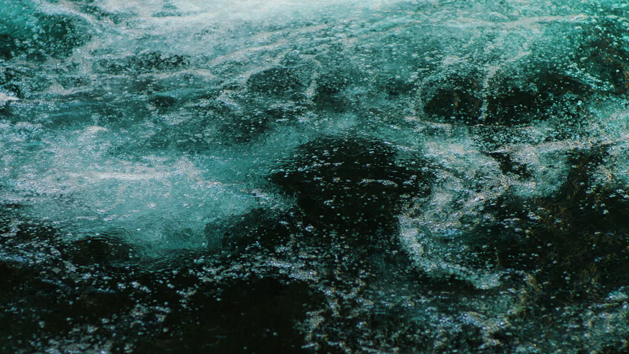 Slow-motion footage of a river with bubbles rising gracefully through clear water. The sunlight illuminates the water, creating vibrant colors and a mesmerizing natural scene