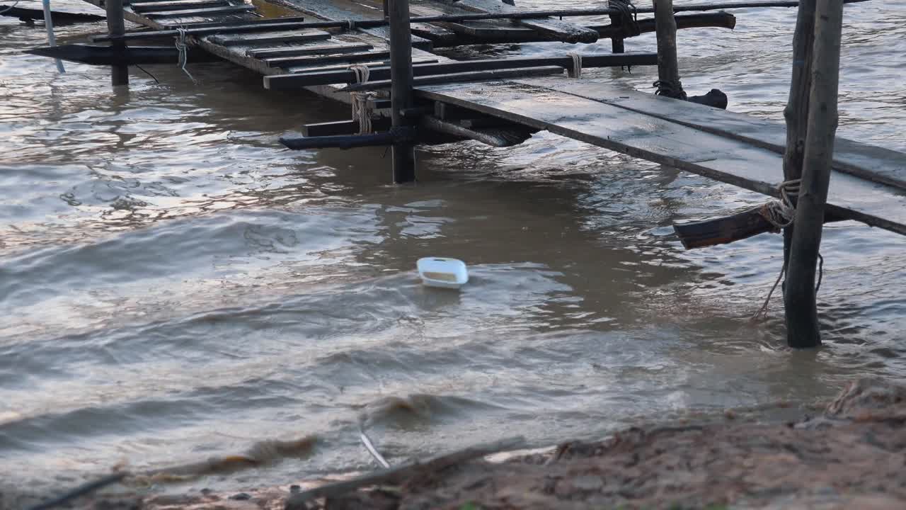 파도가 움직일 때 해안선을 따라 떠다니는 폴리스티렌 조각과 함께 호수로 나가는 오래된 목조 부두의 중간 크기 똥