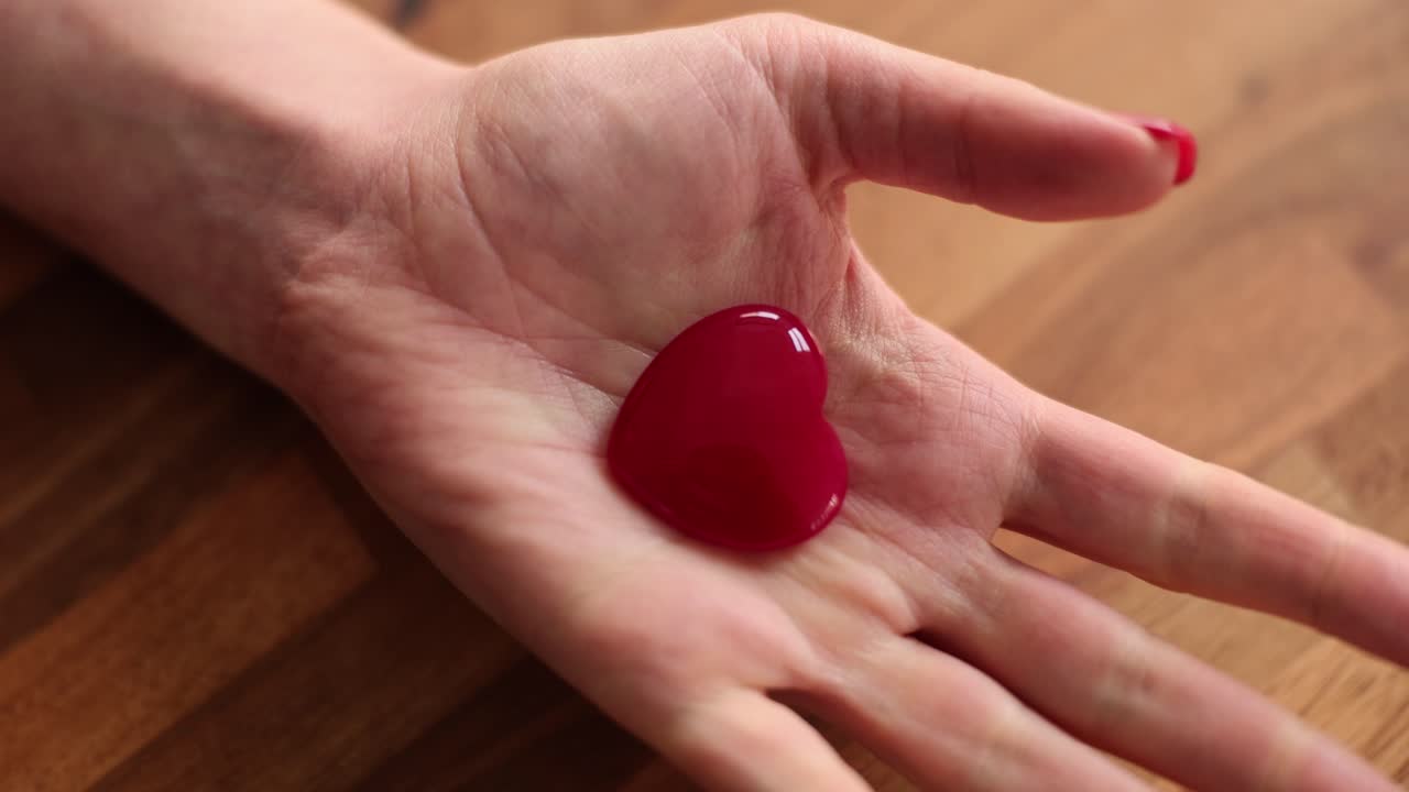 Woman hand with red nails shows small heart toy figure
