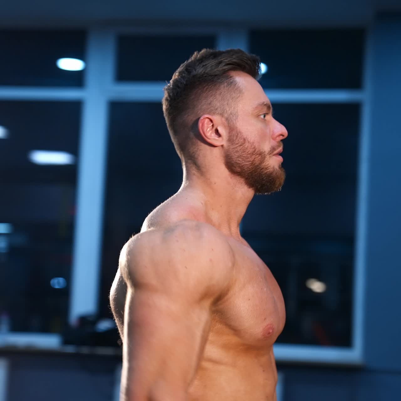 Athletic man in gym is posing to the camera. Bodybuilder with perfect body. Naked torso with perfect abs