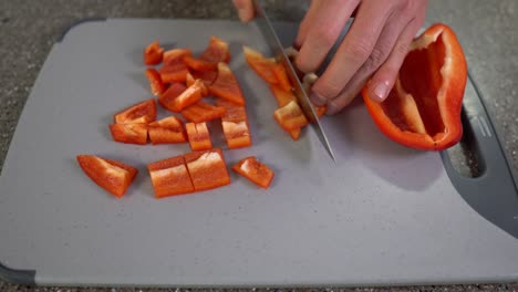 table top view - man hands, cutting red bell pepper with chefs knife on grey chopping board, closeup