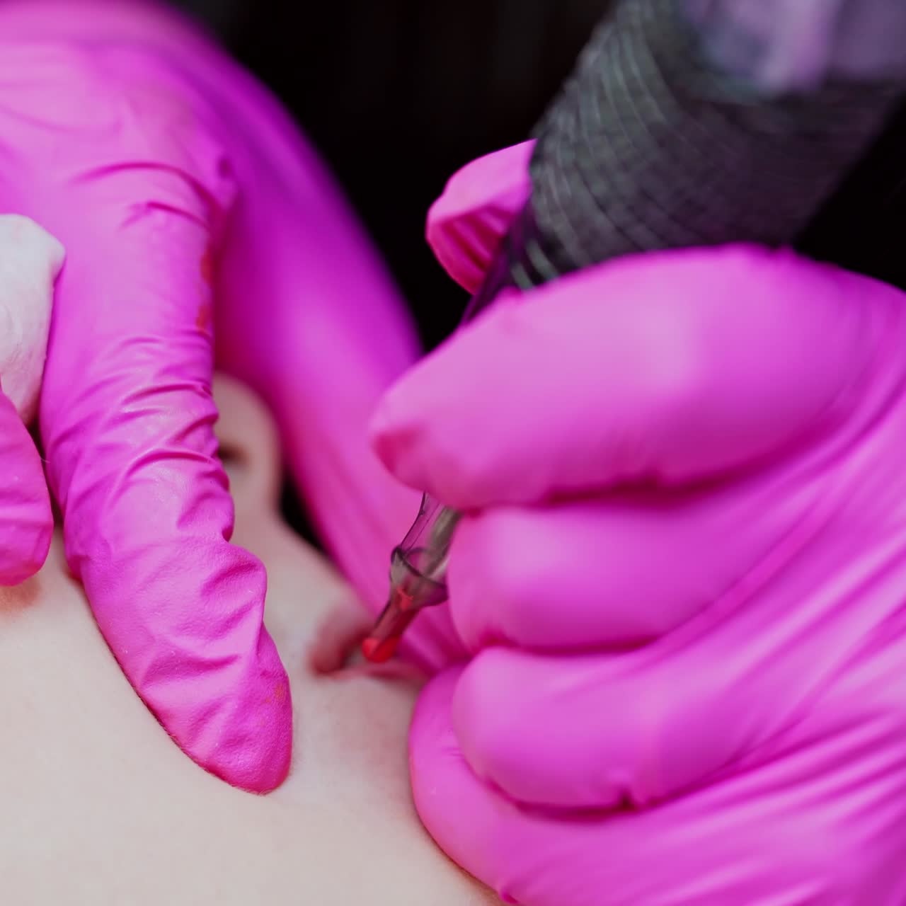 Lips tattoo procedure. Cosmetologist in pink gloves doing lips permanent makeup for female client in a beauty spa. Close-up.