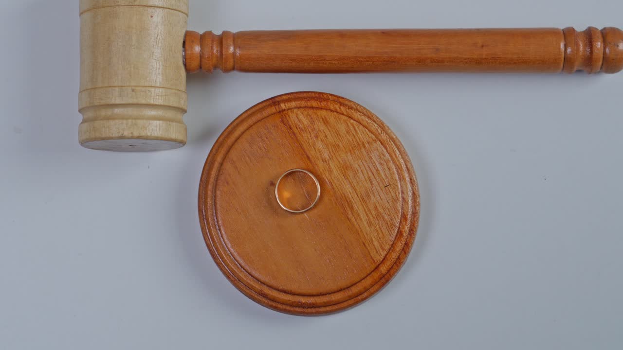 Top view of hand removing two gold wedding rings from judge's gavel block