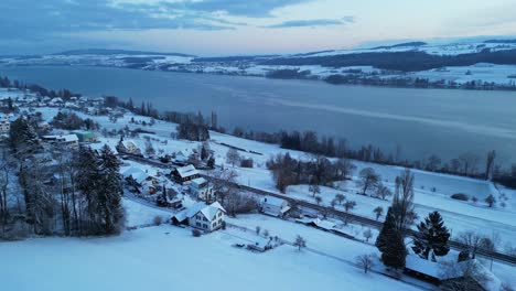 wintry morning with a drone flying over a snow-covered landscape with a lake in switzerland, trees and hills in the background