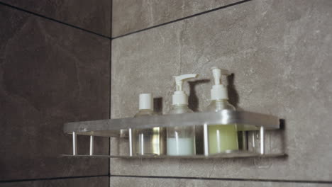 modern bathroom scene with gray stone effect tiles and close up of three transparent cosmetic bottles neatly arranged on metal wall-mounted shelf