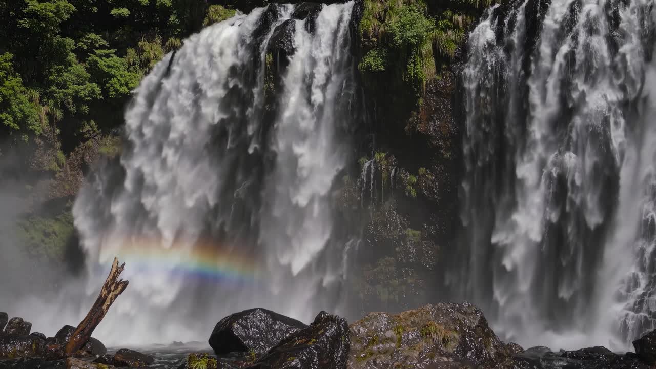 Aerial video captures a lush forest waterfall cascading down rocky cliffs, showcasing vibrant
