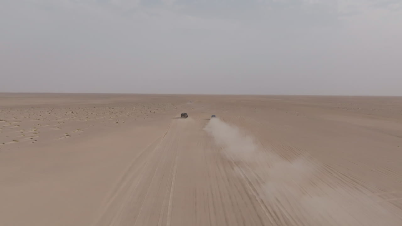 Two off-road cars drive across a vast desert road to Bar Al Hikman, Oman