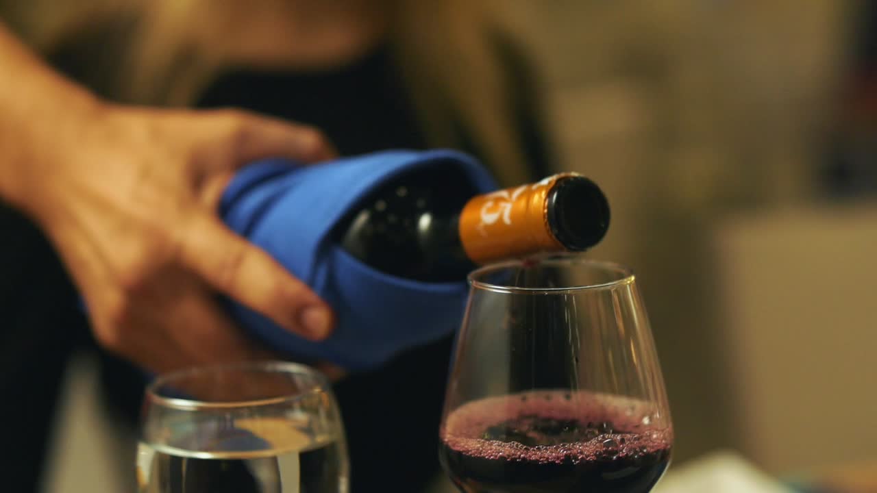 camarero vertiendo vino tinto en una copa de vino en la mesa