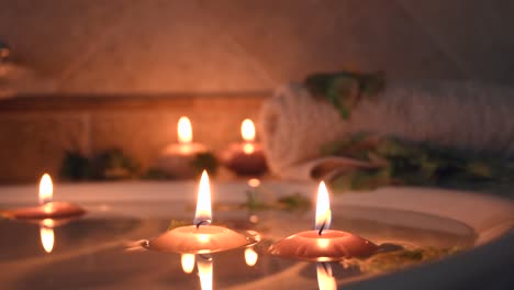 relaxing spa background with candles floating in the bath water, some green petals and a towel near the water surface