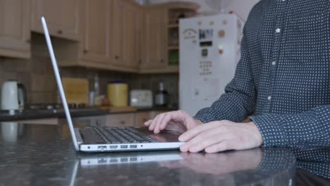 smartly dressed man using the track pad and typing on a laptop on a kitchen counter while working from home