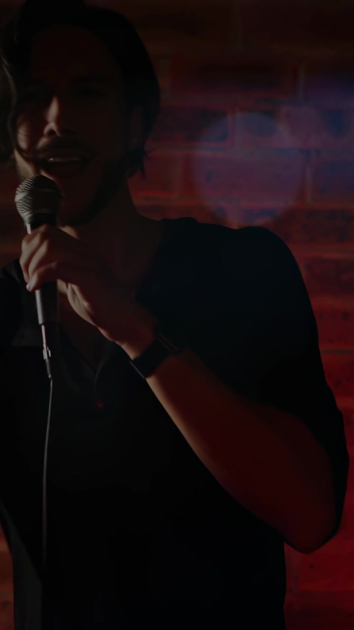 Vertical video: Camera moving up, male performer raising mic, leaning and gesturing, delivering set