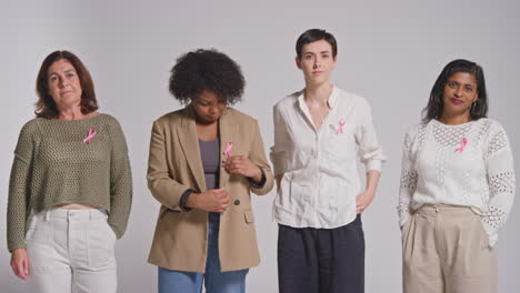 Studio-Portrait-Of-Multi-Racial-Group-Of-Women-Of-Different-Ages-With-Serious-Expressions-Wearing-Pink-Breast-Cancer-Awareness-Ribbons-Against-White-Background-1