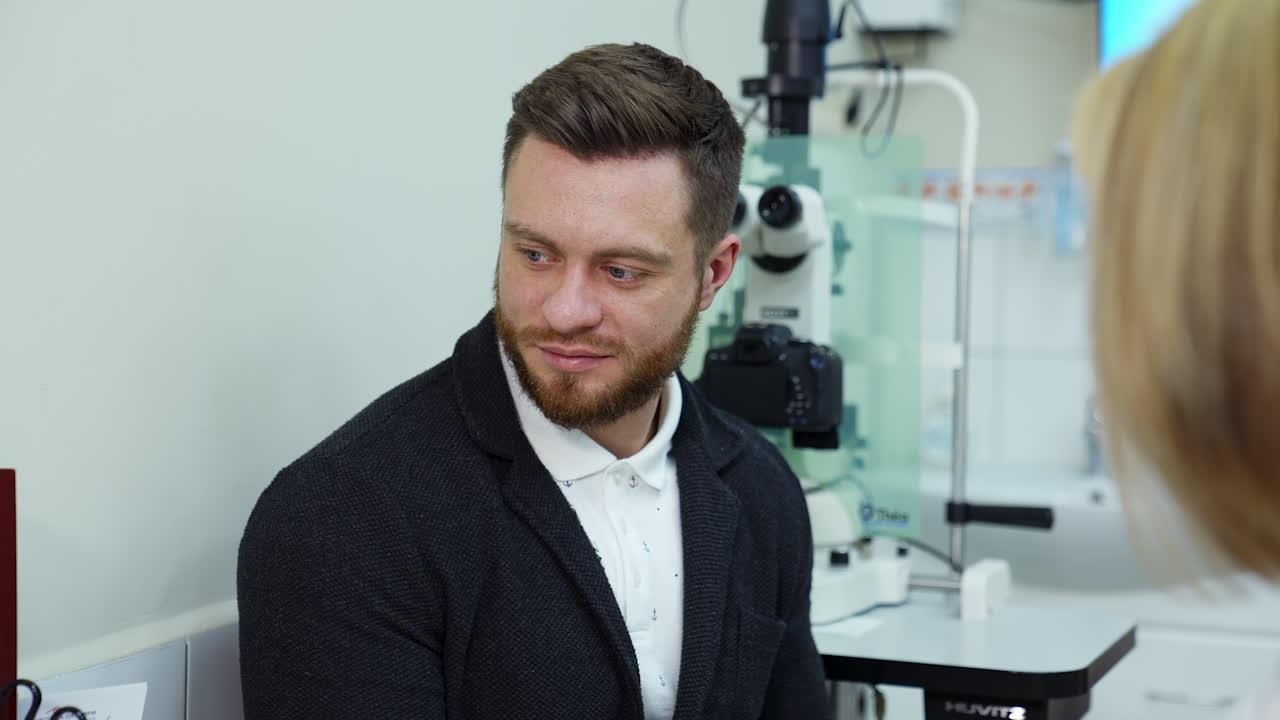 Optician talking to a male patient in clinic. Young handsome man listening to a female doctor in ophthalmology center.