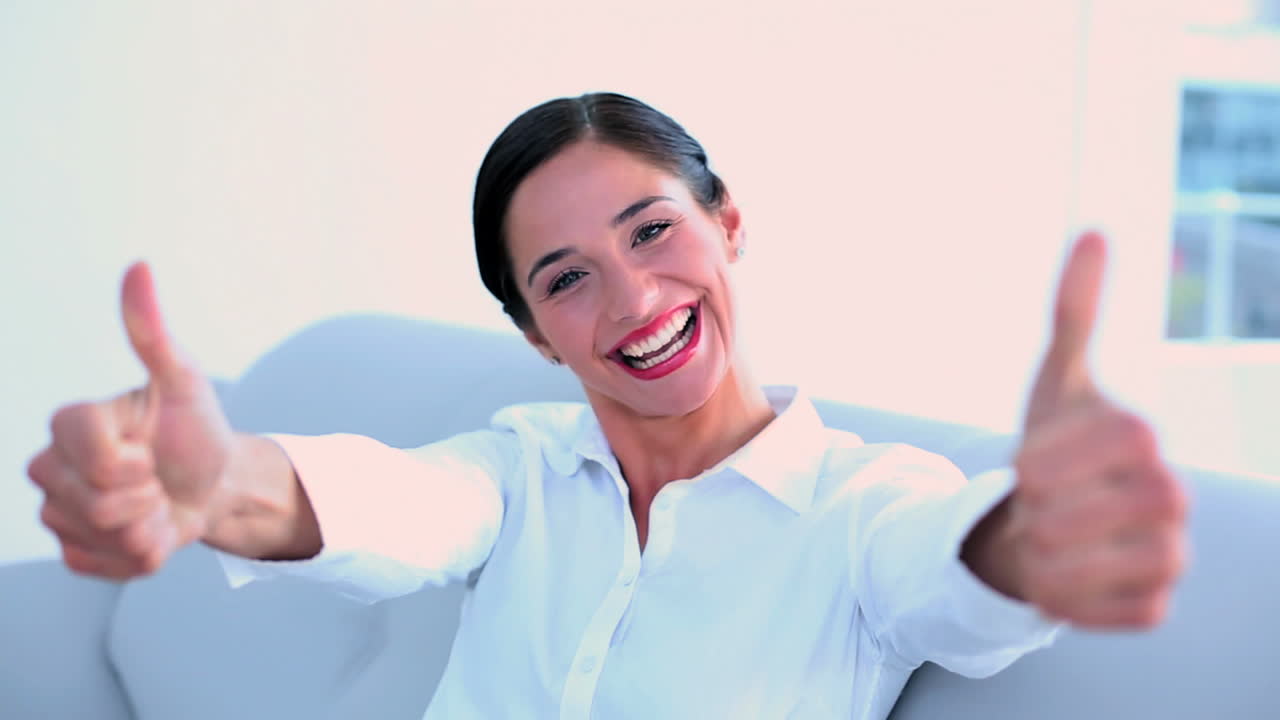 mujer de negocios exitosa sentada en el sofá y dando pulgares a la cámara