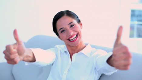 Successful-businesswoman-sitting-on-couch-and-giving-thumbs-up-to-camera