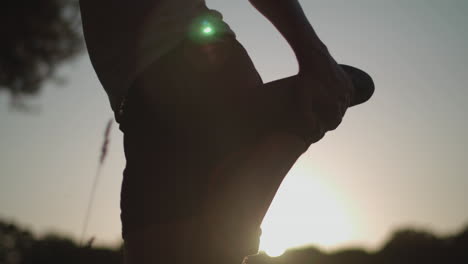 close up shot of man in park stretching out legs before going for a run whilst being silhouetted by the sun, in slow motion