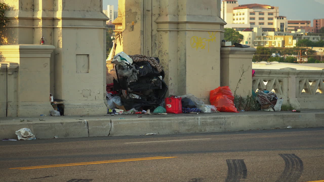 View of bags full of trash piled up on the sidewalk of 6th st bridge,California, USA with cars passing by in high speed
