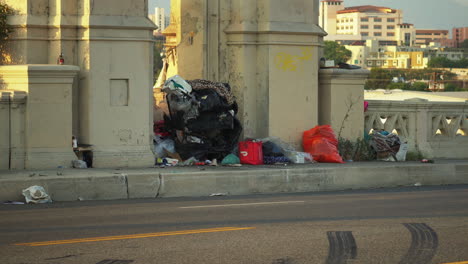 view of bags full of trash piled up on the sidewalk of 6th st bridge,california, usa with cars passing by in high speed