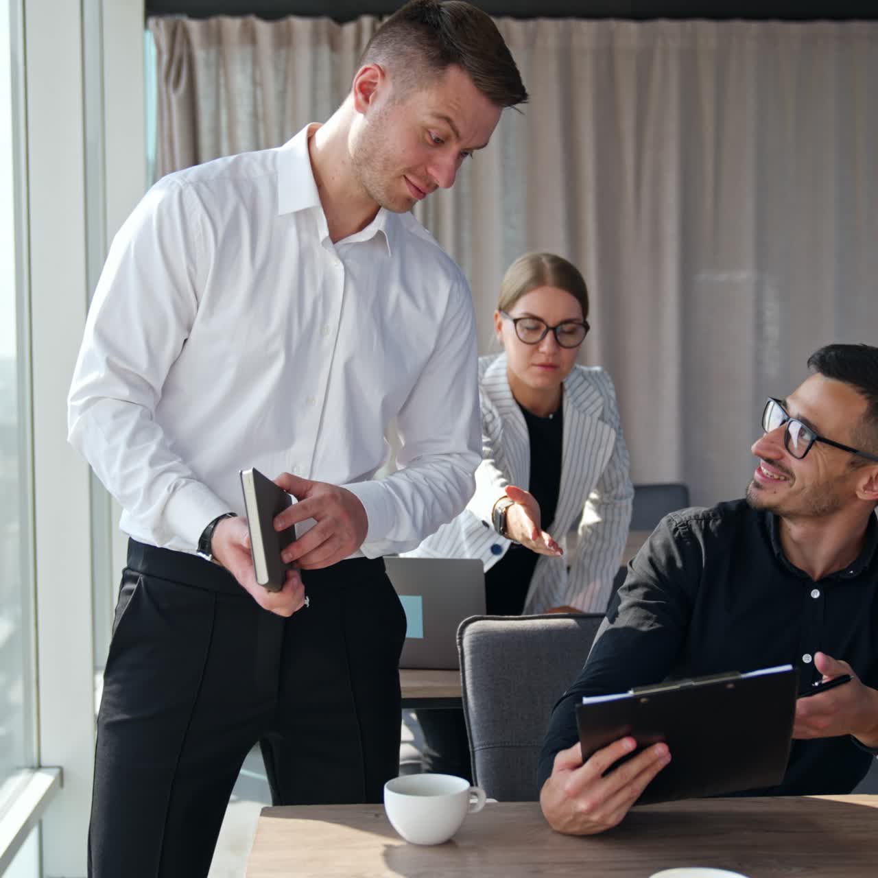 Office team discussing the documents. Men at the first desk hold the folder and female employee behind making suggestions pointing at papers