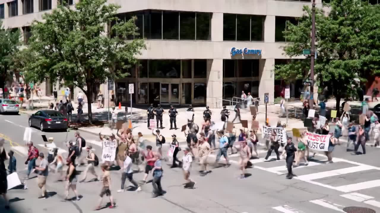 Large Group of Protesters Marching Through City Street with Signs Demanding Justice and Equality, Escorted by Police Officers in Uniform