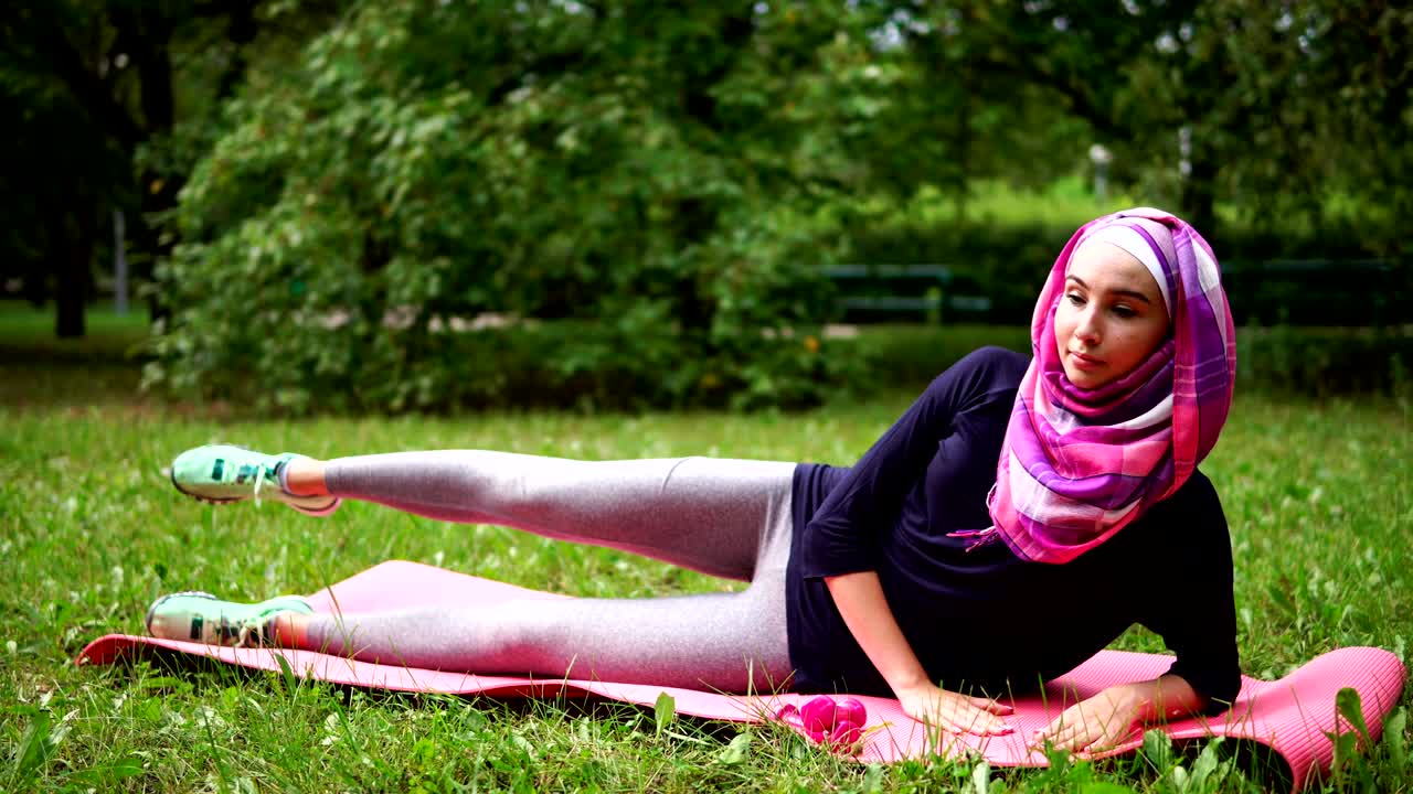 Young Muslim woman in burqa doing strengthening exercises for hip muscles