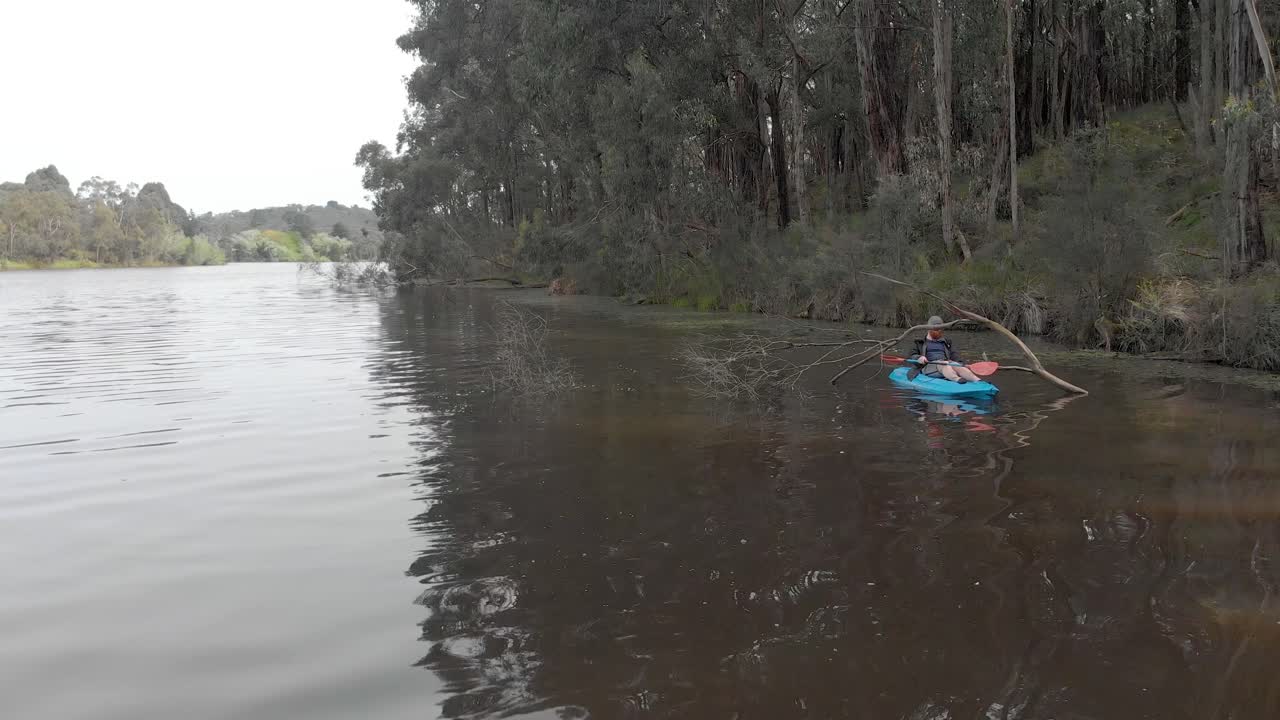 Un uomo barbuto che passa sotto un albero sommerso sulle rive di un fiume nell'Australia meridionale