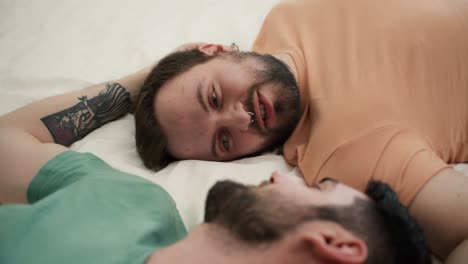 portrait of attractive bearded gay men couples lying on bed together, talking