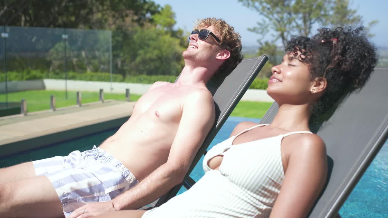Couple reclining chairs poolside man shifting, raising shades, smiling, greeting woman in swimsuit
