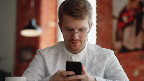 Un-Hombre-Atractivo-Con-Gafas-De-Pie-Solo-En-El-Interior-Sosteniendo-En-Las-Manos-El-Número-De-Marcación-Del-Teléfono-Inteligente-En-La-Pantalla-Táctil.-Mujer-Joven-Y-Alegre-Navegando-Por-Internet,-Navegando-Por-Internet,-Elige-El-Concepto-De-Compra-De-Productos-En-Línea