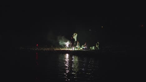 family celebrating with fireworks by the lake at night