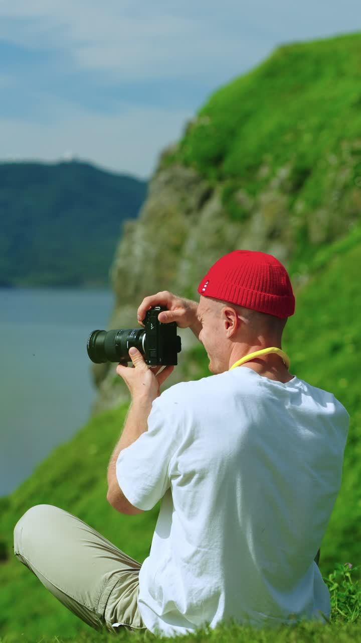 Uomo con berretto rosso che fotografa un panorama suggestivo su una collina erbosa
