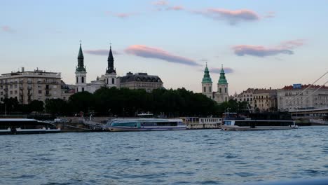 River-ferry-cruise-traverse-the-Danube-River-in-Budapest,-Hungary-during-a-beautiful-twilight-golden-hour-evening